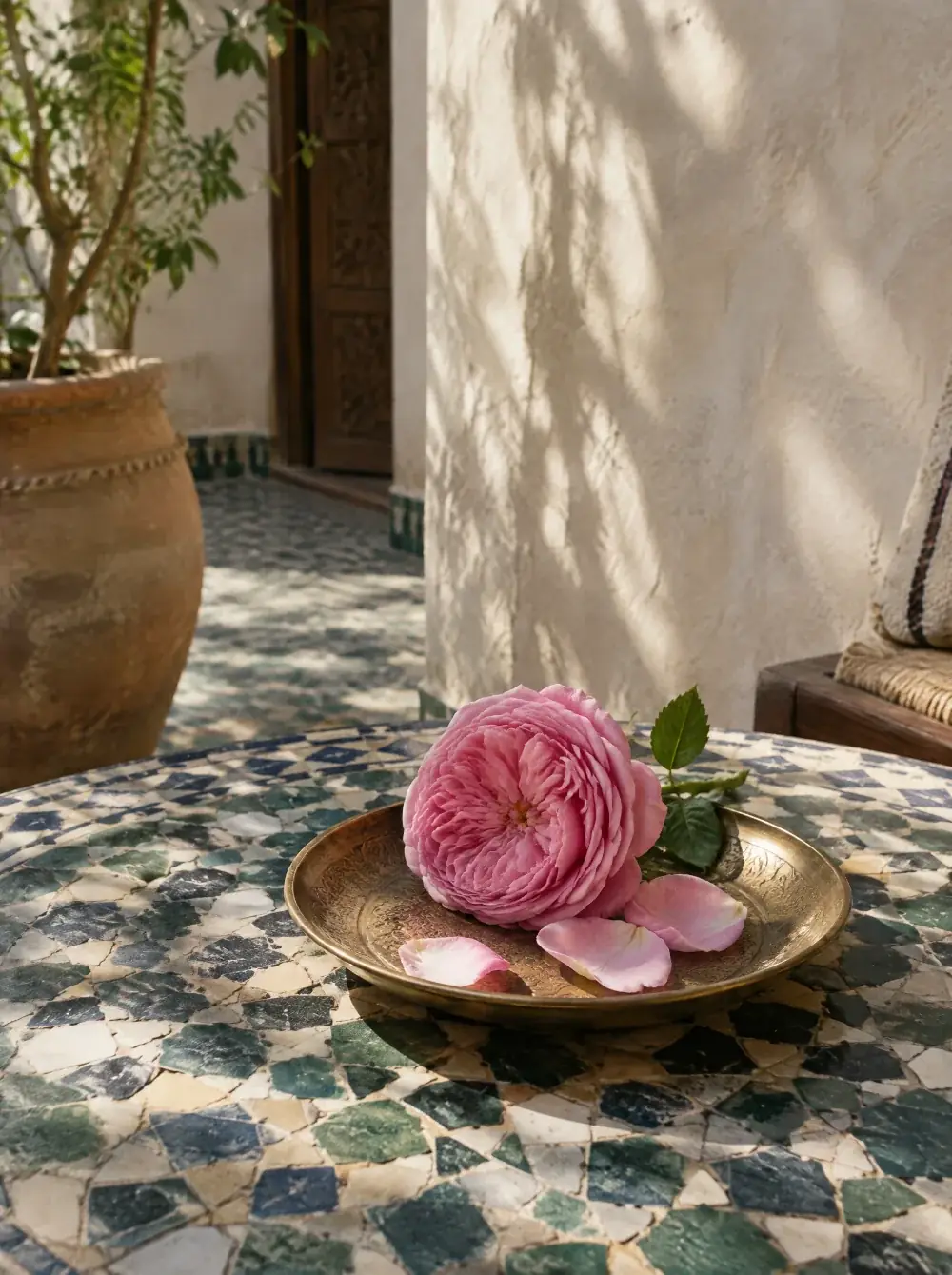 Rose de Damas et quelques pétales sur une coupelle en laiton, posée sur une table en zellige